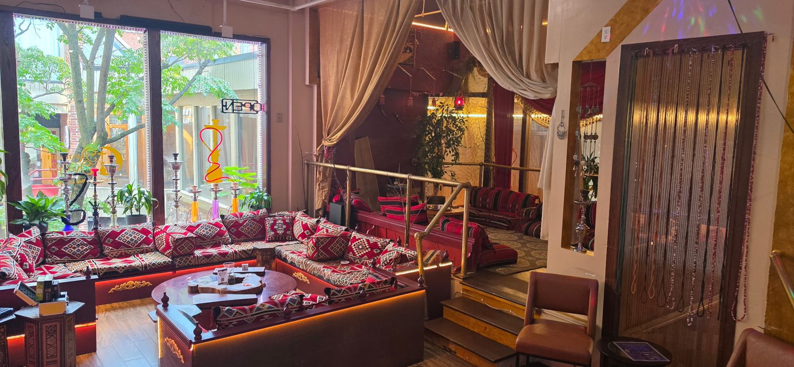 Main lounge with patterned floor seating and hookahs lined up in the front windows